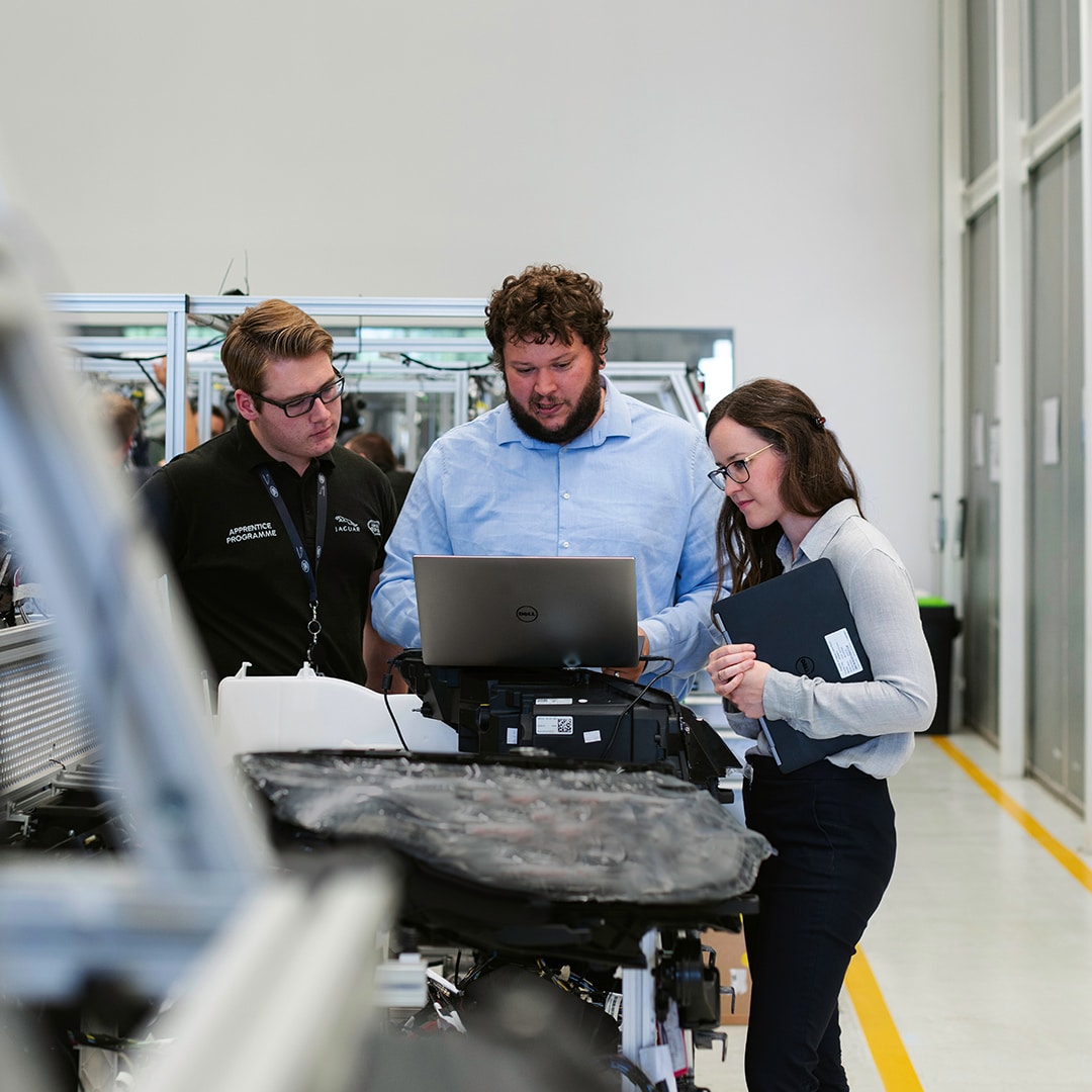 To mænd og en kvinde ser på en computerskærm i en fabrik
